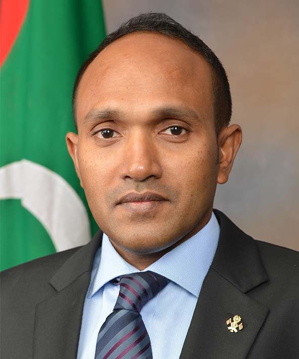 Dr Mohamed Jameel Ahmed in a dark suit, photographed against the national flag of the Maldives.