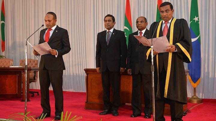 A wider view of the swearing-in: Dr Jameel at the microphone reading the oath, the judge administering it at the right.