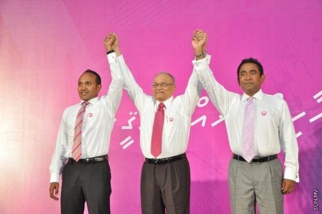 Three men on a stage with their joined hands raised above their heads before a crowd.