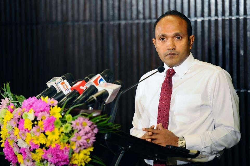 Dr Jameel standing at a lectern behind a bank of broadcast microphones.