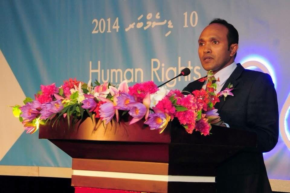 Dr Jameel speaking from a flower-dressed lectern in front of a backdrop reading Human Rights, 2014.