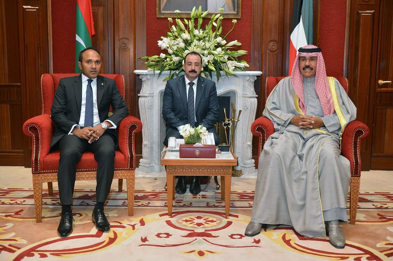 Dr Jameel seated in a gilt chair opposite his hosts in a state reception room, Kuwaiti flags behind.